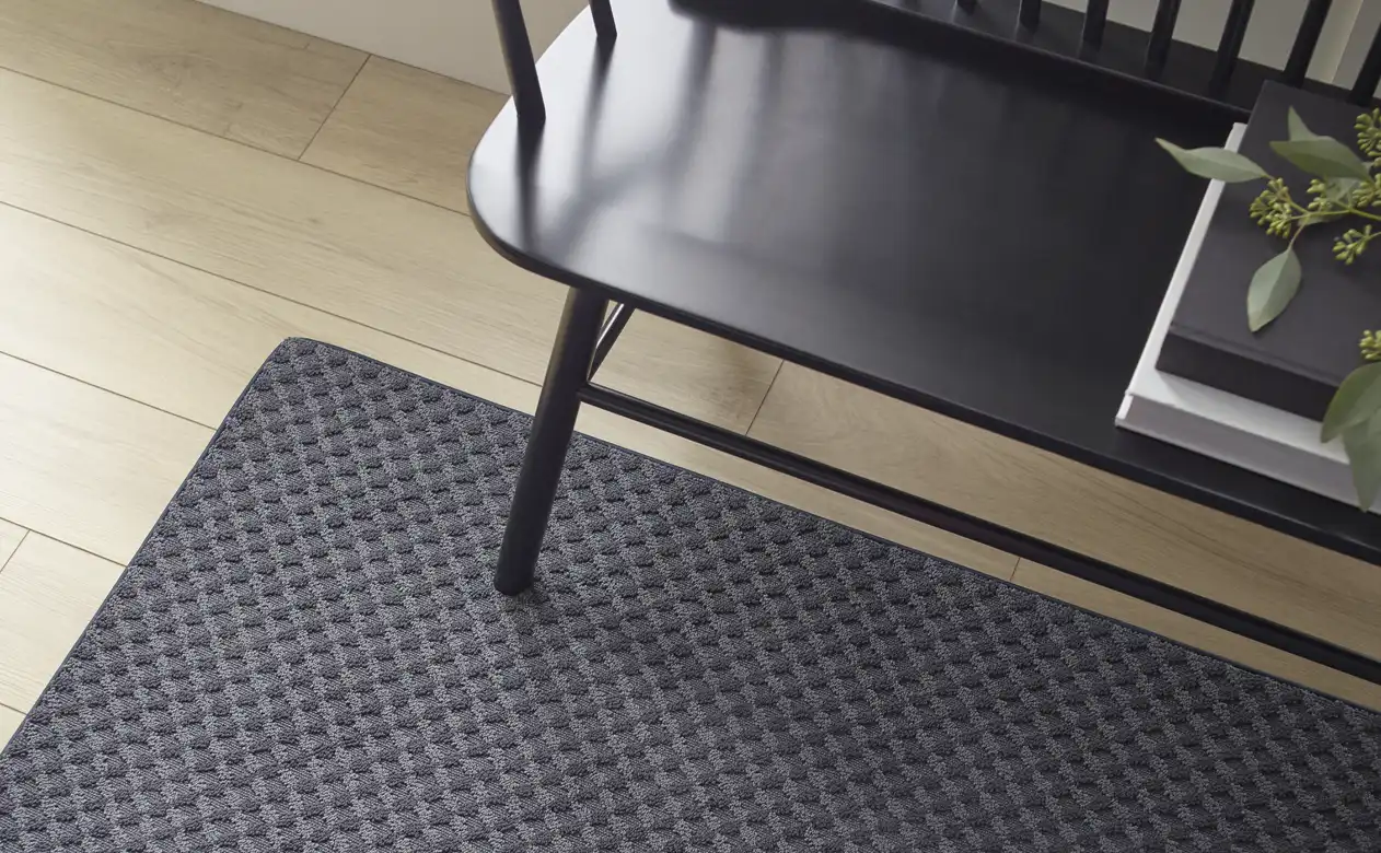 black textured area rug in hallway with light wood floors and black wood bench